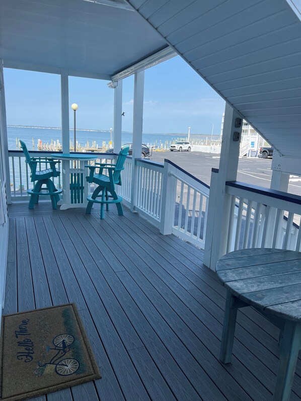 A wooden deck with a table and chairs, overlooking a body of water and a pier.