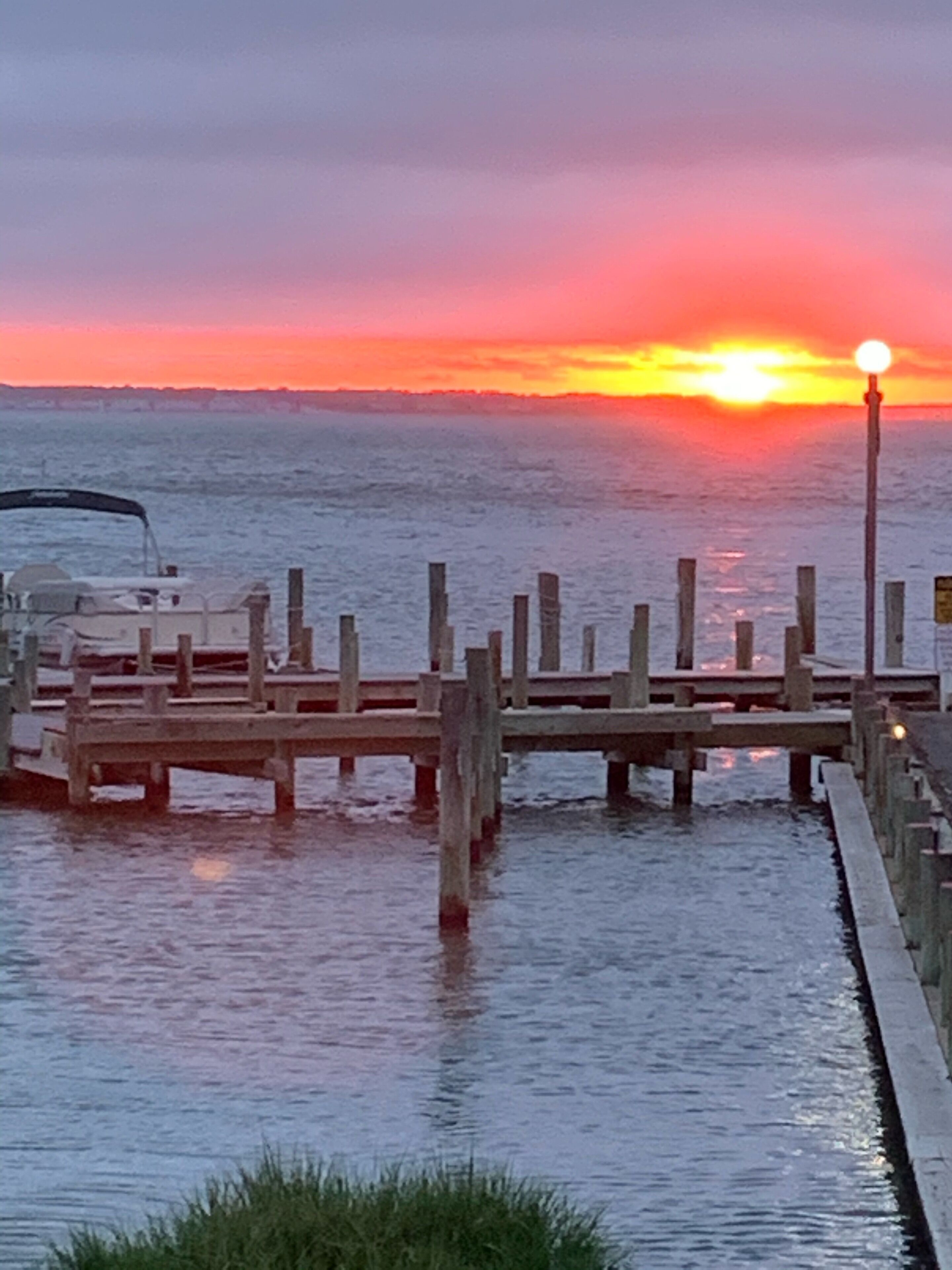 A wooden pier extending into calm water with a sunset in the background.