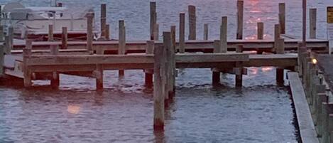 A wooden pier extending into calm water with a sunset in the background.