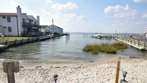 A beach with a pier extending into calm waters, a sandy shore, and a building with a white facade. - 1st Floor Bayfront 1 bedroom Updated Condo with pool overlooking the bay!! (Ocean City)