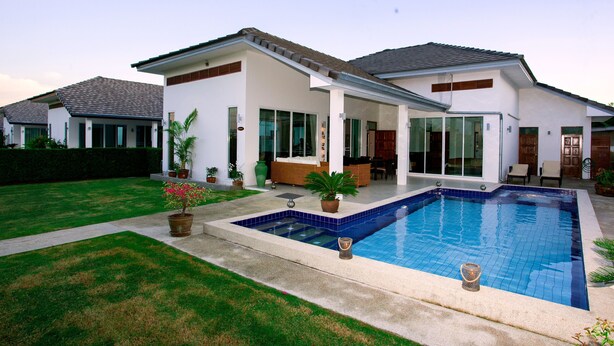 Une maison moderne dotée d’une piscine, d’un patio couvert et d’une pelouse bien entretenue.