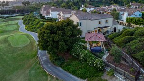 Un quartier résidentiel avec des maisons, un terrain de golf et une grande maison dotée d’un toit recouvert de tuiles rouges et d’un patio.