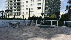 Una terraza en la azotea con mobiliario exterior, piscina y vista a un edificio de gran altura.