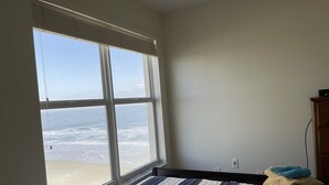 Un dormitorio con un ventanal grande que da a la playa, una cama con ropa de cama a rayas y una mesita de noche de madera con toallas.