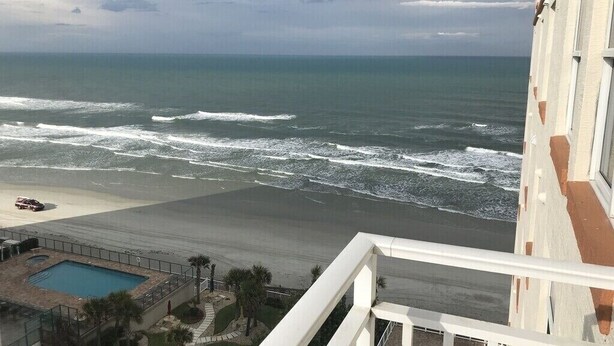 Vista de una playa desde un balcón con piscina y un edificio al frente.