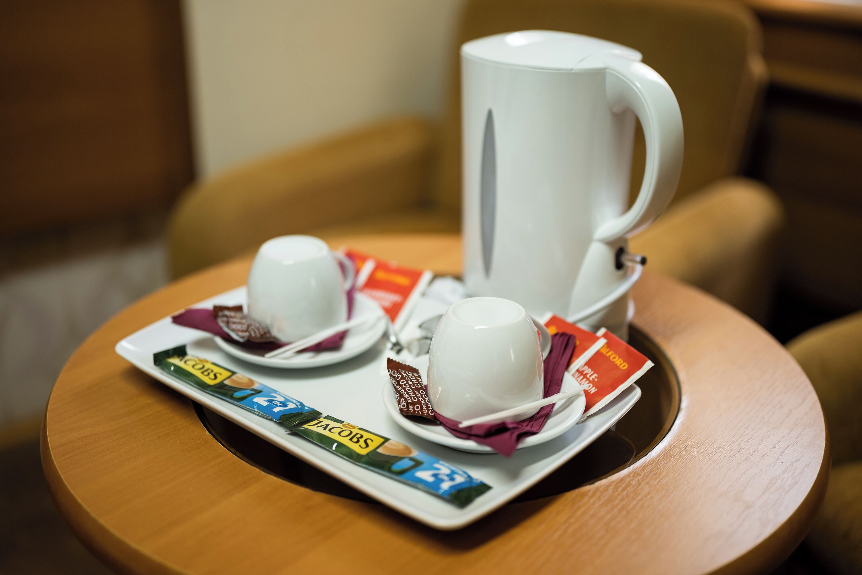 Een dienblad met twee kopjes koffie, een mok en twee pakjes koffie van Jacobs op een houten tafel.