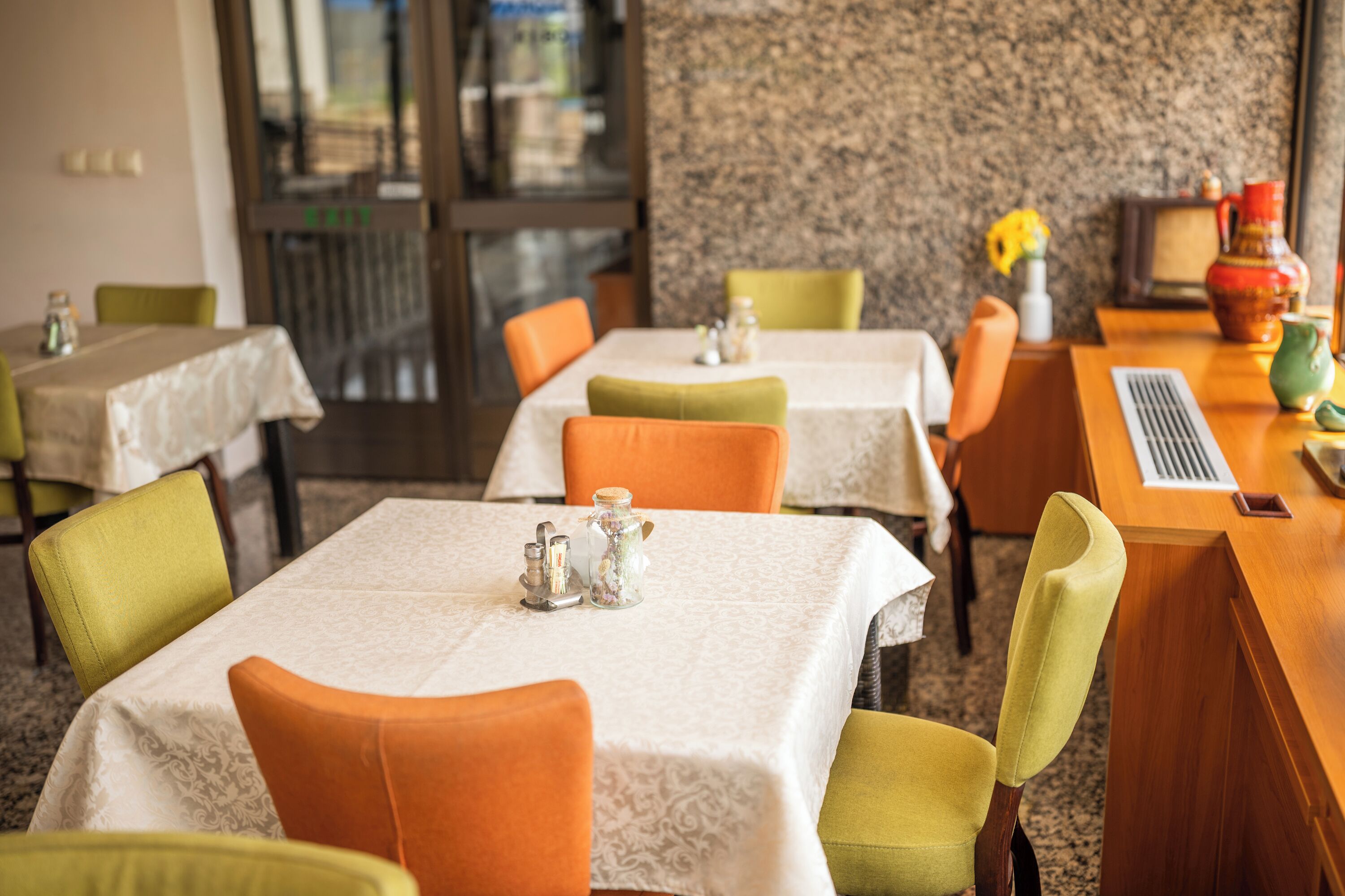 A restaurant interior with multiple tables and chairs, some with white tablecloths and others with plain surfaces.