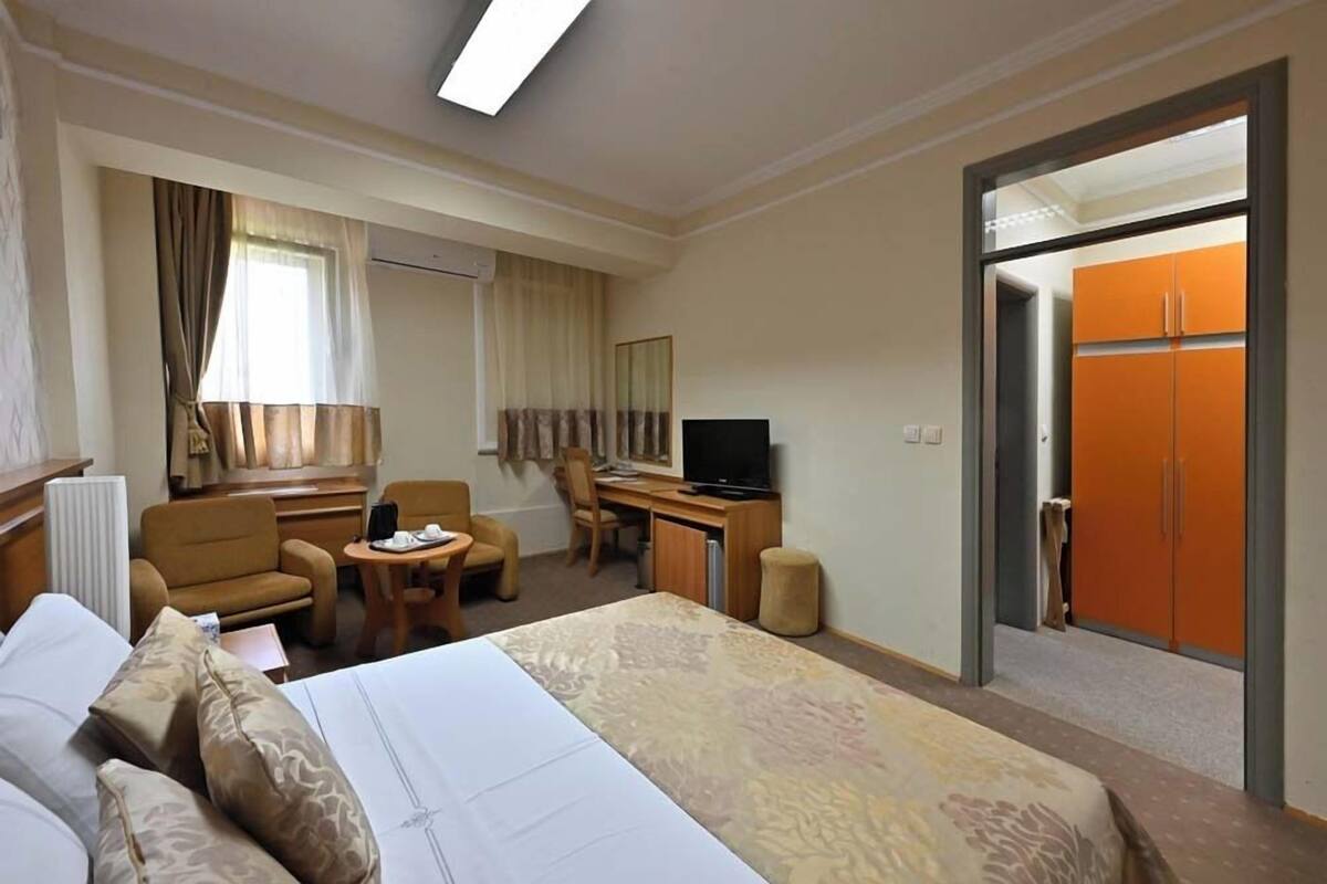 A hotel room with a bed, a desk with a computer, a TV, and a wardrobe.