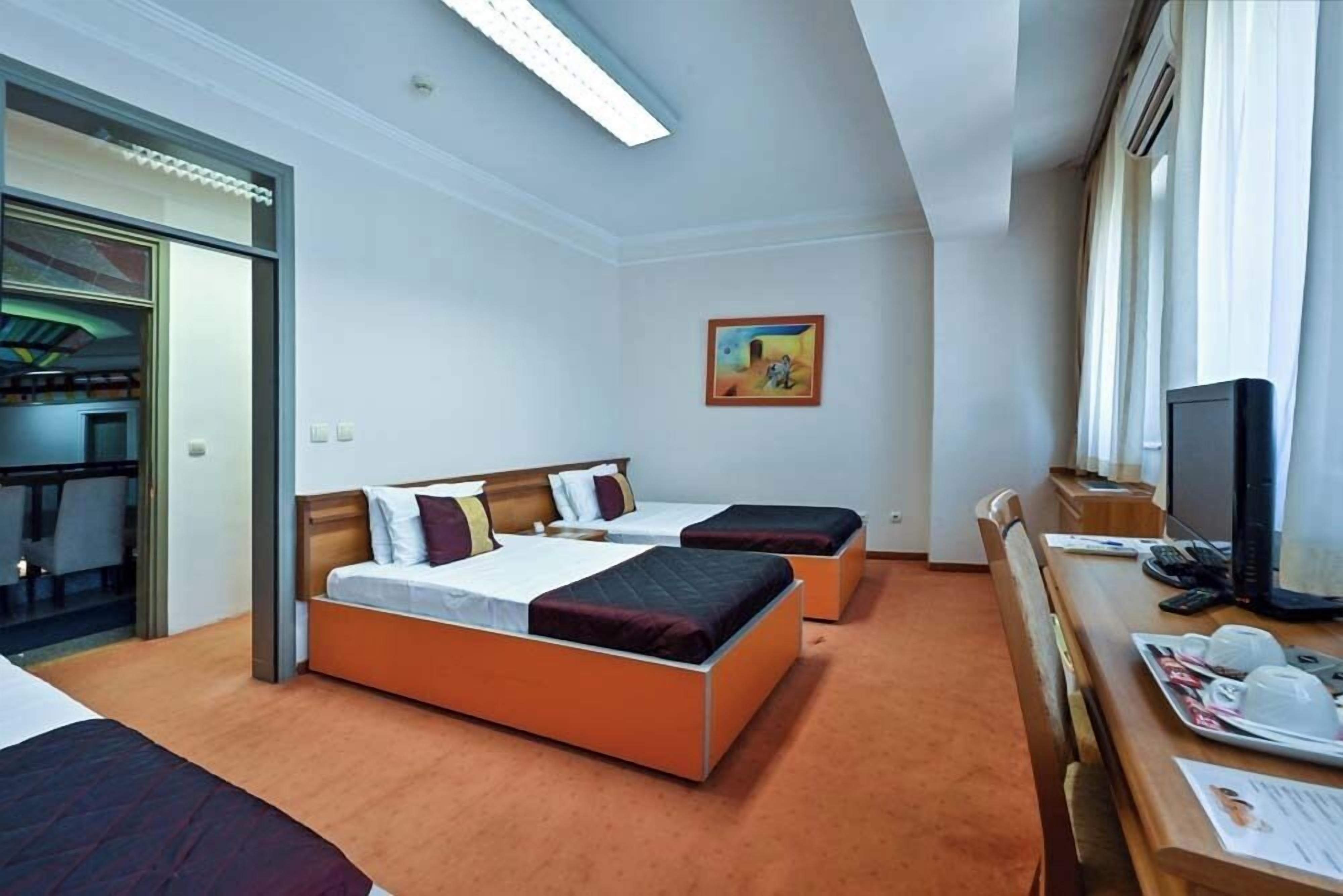 A hotel room with two beds, a desk with a computer, and a window with curtains.