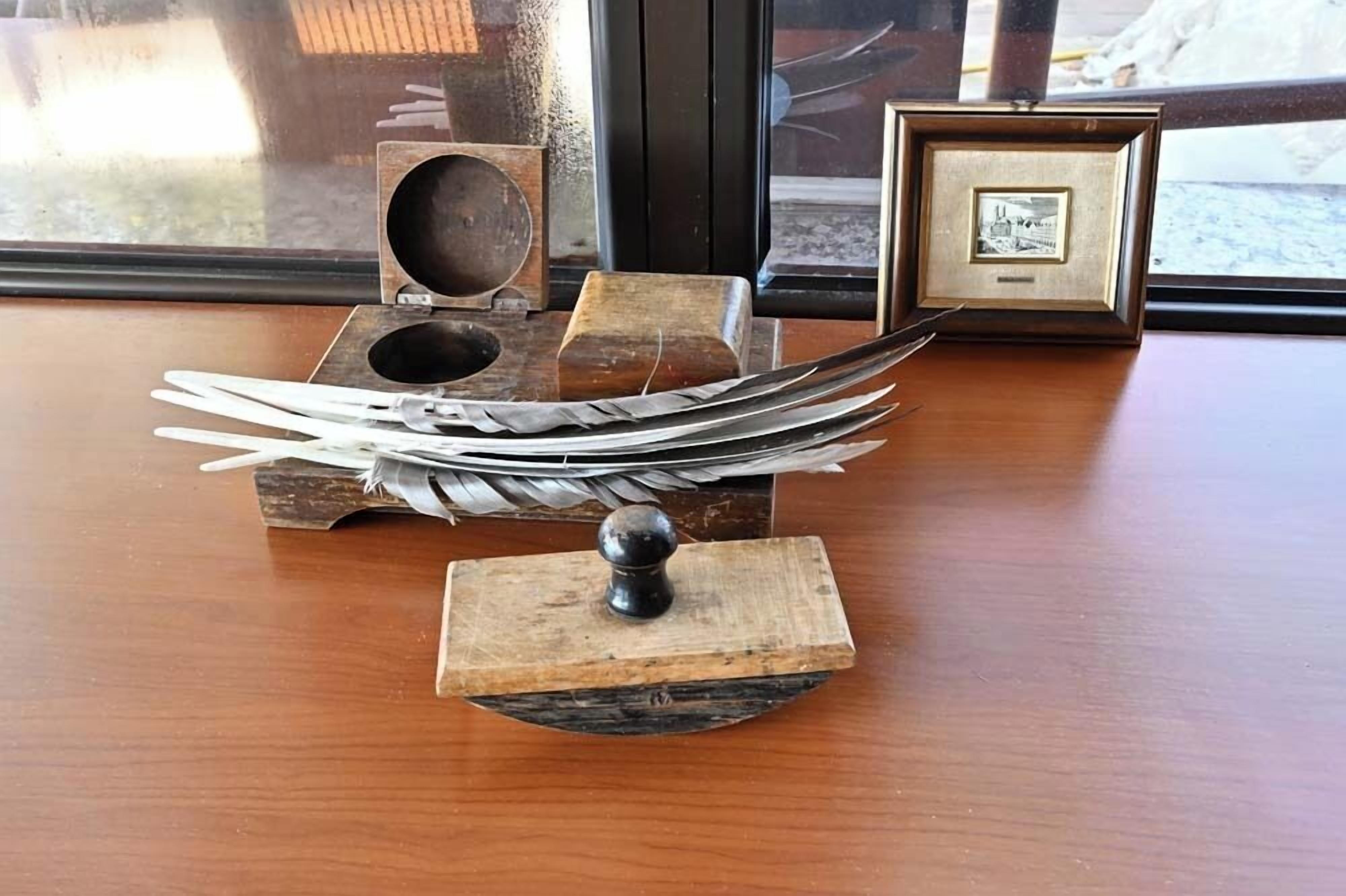 A wooden table with a vintage feather quill holder and a framed picture.