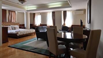 A hotel room with a bed, a desk, a dining table with chairs, and a large window with curtains.