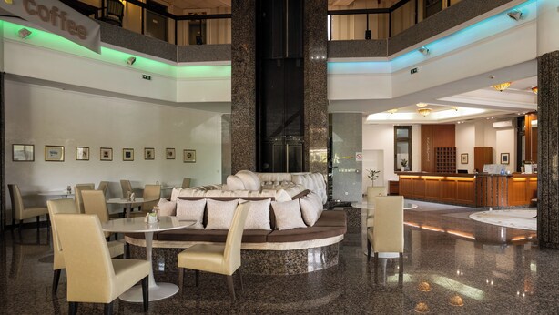 A lobby with a central seating area, a reception desk, and framed pictures on the walls. - Hotel Sole Mio (Novi Sad)