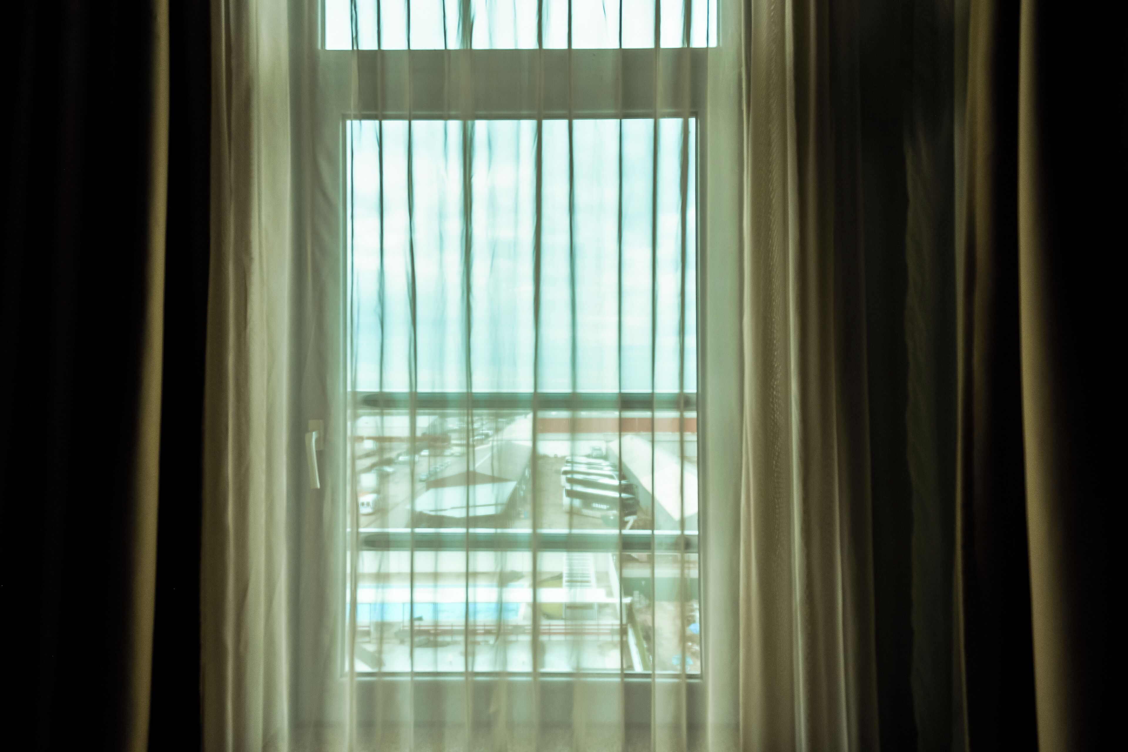 A window with vertical blinds, a view of a building outside, and curtains partially drawn.