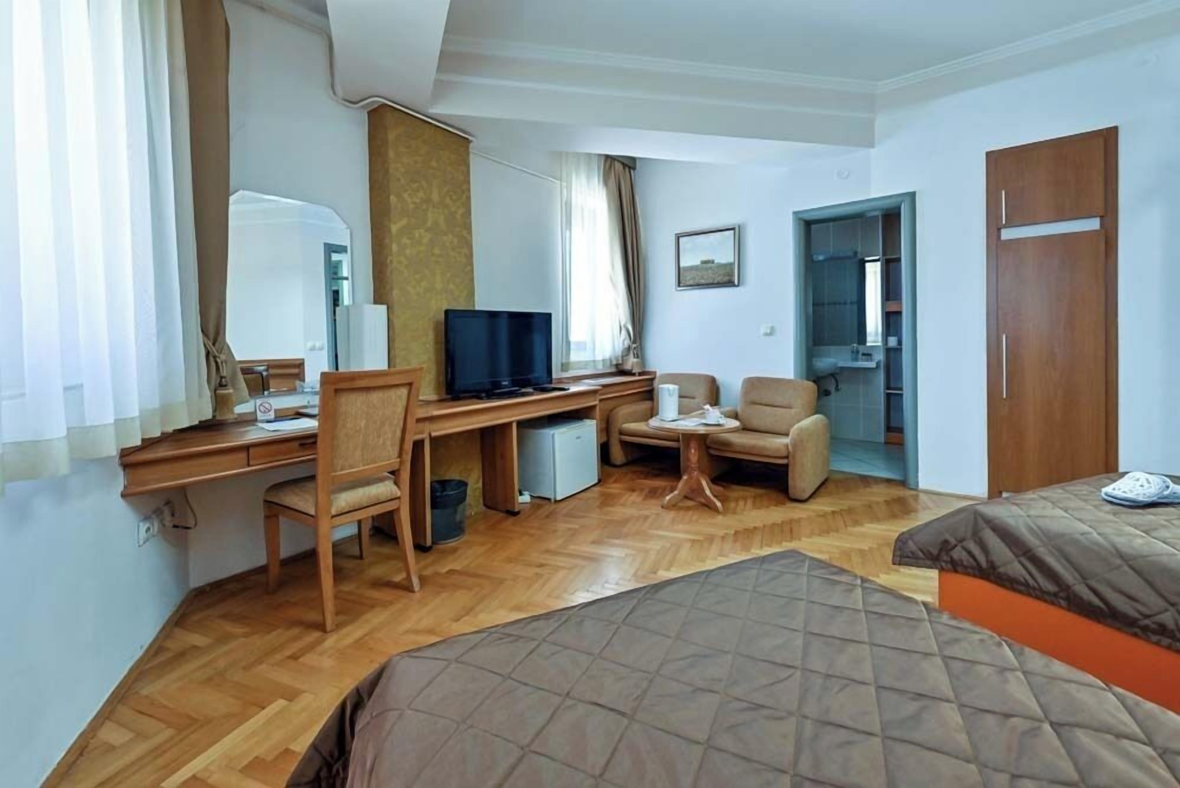 A hotel room with a wooden desk, a television, a chair, a bed, and a wardrobe.