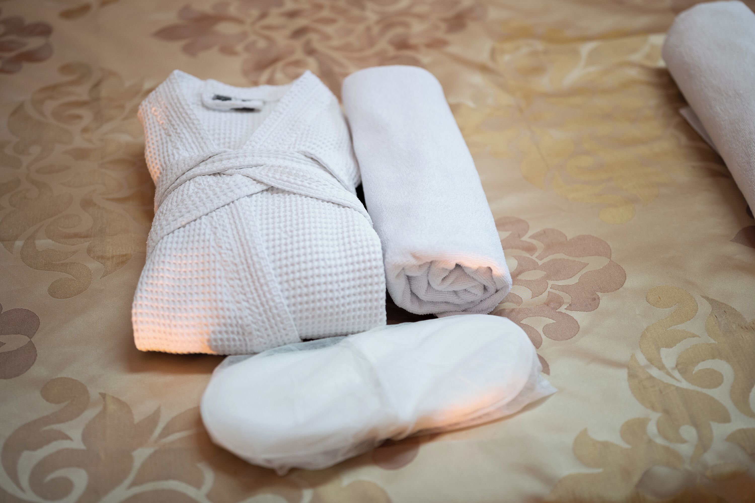 Una toalla blanca doblada con cuidado y una bata sobre una cama con una colcha estampada.