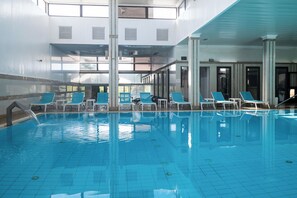 Une piscine intérieure à l’eau d’un bleu cristallin, entourée de murs blancs et de grandes fenêtres.