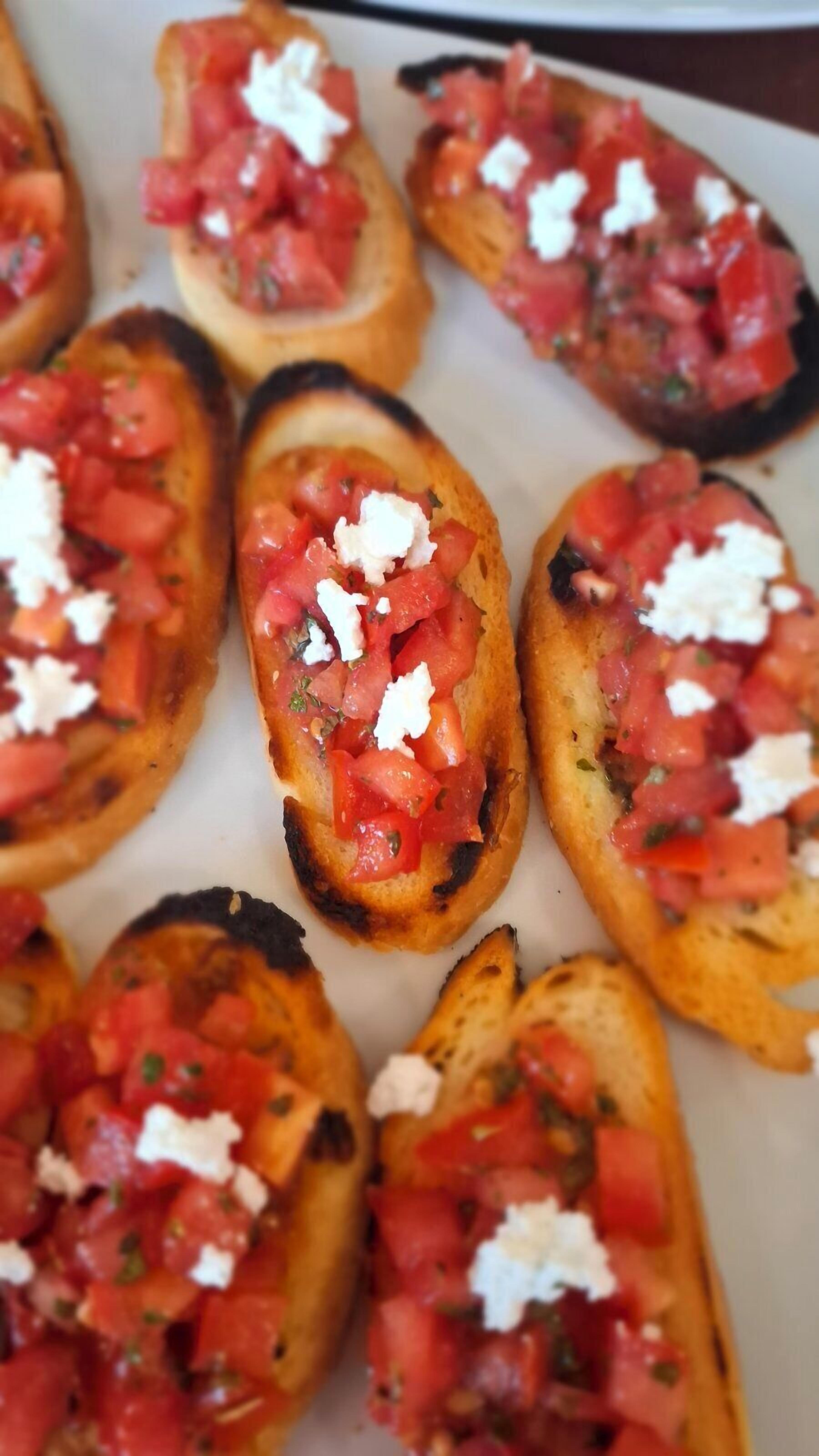 A tray of grilled bread topped with tomatoes and feta cheese.
