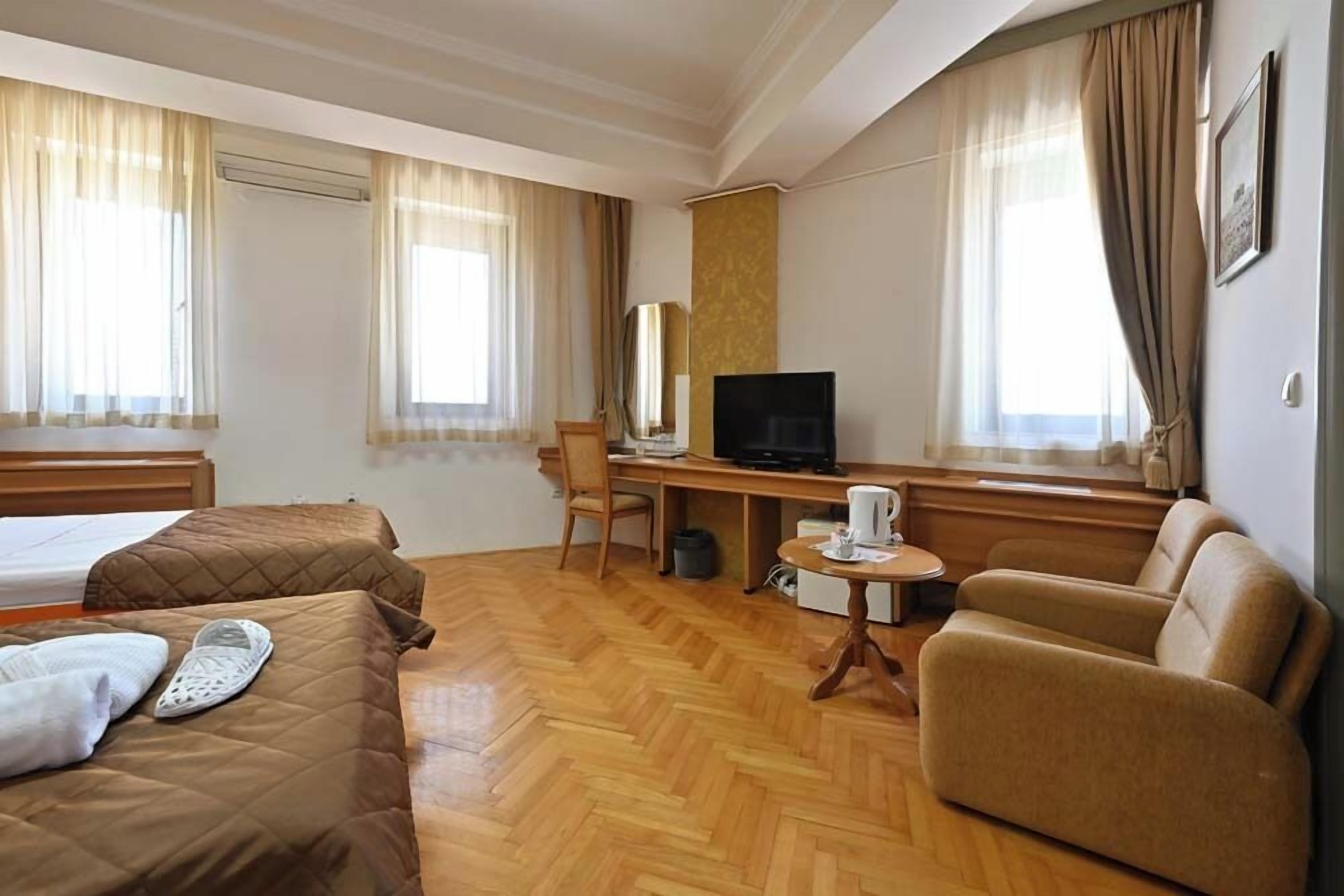 Una habitación de hotel con dos camas, un escritorio con televisor, una silla y un sofá.