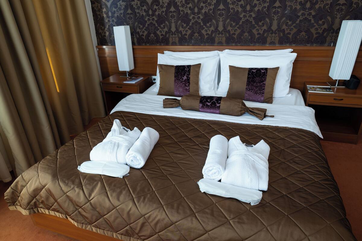 A hotel room with a brown quilted bedspread, neatly folded towels, and a wooden headboard.
