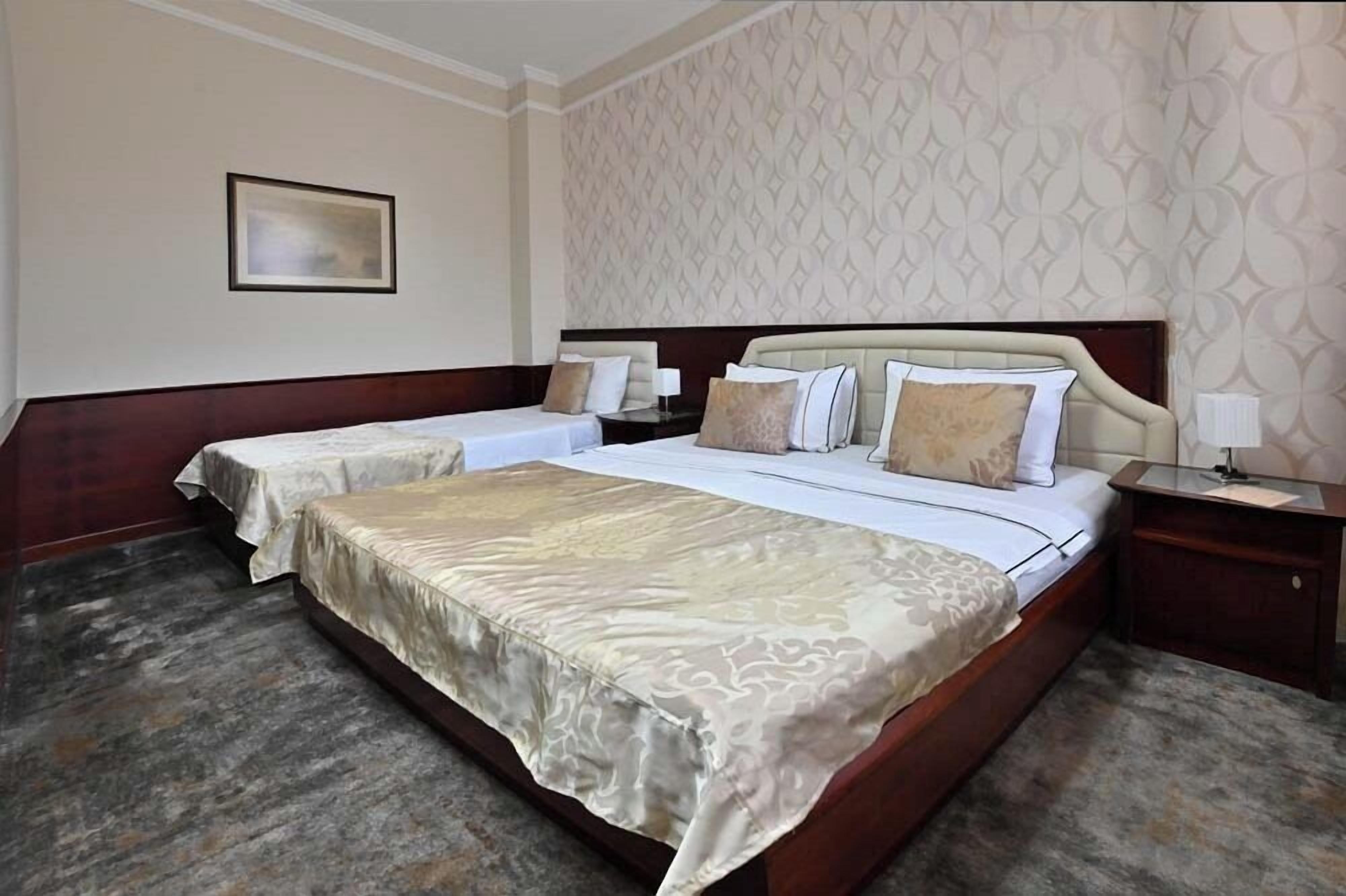 A hotel room with a large bed, two smaller beds, a nightstand, and a framed picture on the wall.