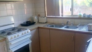 A compact kitchen with white cabinets, a gas stove, a built-in oven, a sink, and a window with a view of the outside.
