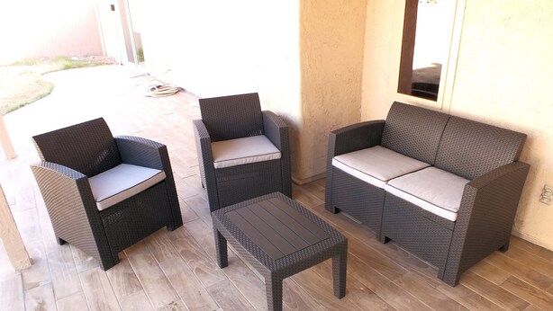 Een patio met rieten meubels, waaronder een bank, twee stoelen en een bijzettafeltje.