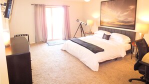 Hotelkamer met een bed, een bureau, een stoel, een plafondventilator, een telescoop en een schilderij aan de muur.