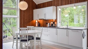 A modern kitchen with white cabinets, a dining table with chairs, and a large window offering a view of the outdoors. - Cozy home in Skollenborg with kitchen (Skollenborg)