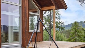 A wooden deck with a swing set, a large window, and a view of a forested mountain range. - Cozy home in Skollenborg with kitchen (Skollenborg)