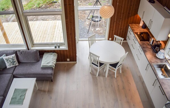 Eine moderne Küche mit Esstisch und Stühlen, einem eingebauten Backofen und einem großen Fenster mit Blick auf eine Terrasse.