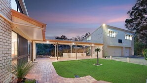 A modern house with a covered patio, a well-maintained lawn, and a brick pathway leading to the entrance. - Serendipity Gardens! (Joyner)