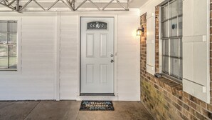 A white front door with a glass panel, a doormat with "Happy Halloween," and a brick wall with a window. - Grill, Relax, or Play at Home Away From Home (Shreveport)