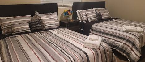 Une chambre d’hôtel avec deux lits, chacun doté de draps et d’oreillers à rayures, une table de chevet avec un vase de fleurs et une fenêtre avec des stores.