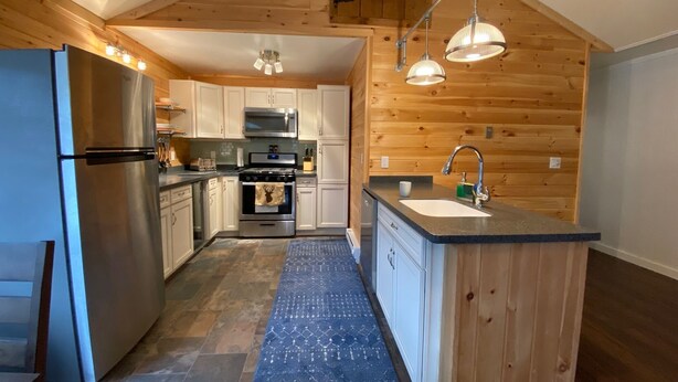 A compact kitchen with white cabinets, a stainless steel refrigerator, a microwave, and an oven. There is a wooden ceiling and a blue rug on the floor. - Newly Renovated AC 4 ACRES 3000sqft home with Full Game Room (Hunter)