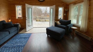 A cozy cabin interior with a wooden interior, a large clock on the wall, and a view of a wooden deck outside. - Newly Renovated AC 4 ACRES 3000sqft home with Full Game Room (Hunter)