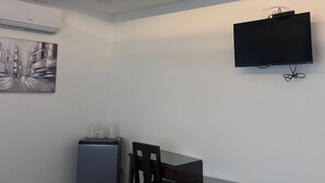 A hotel room with a flat-screen TV mounted on the wall, a small refrigerator, a desk with a chair, and a painting on the wall. - Hotel Naralit (Tilaran)