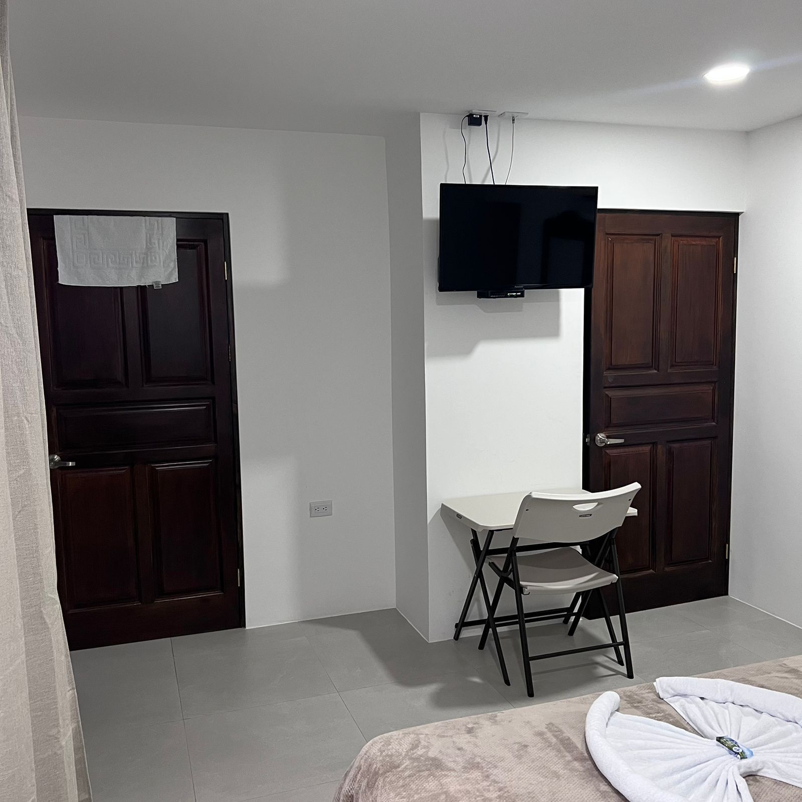 A small, clean room with a desk, chair, and a flat-screen TV mounted on the wall.
