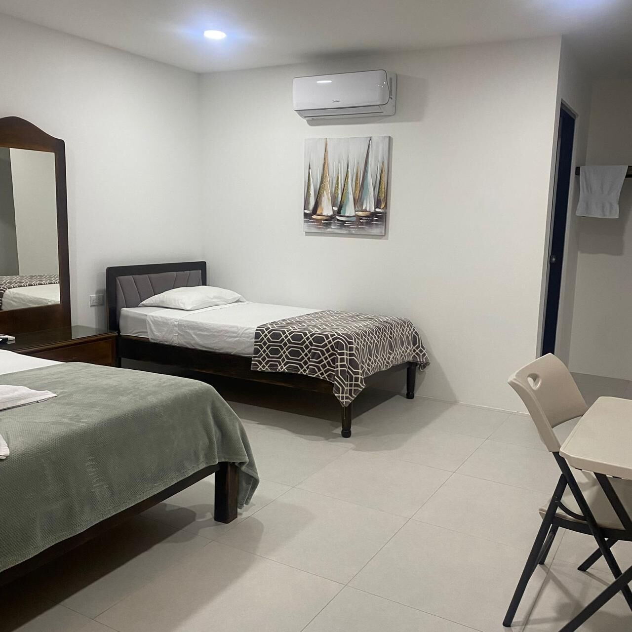 A hotel room with two beds, a desk, a chair, an air conditioner, and a mirror.