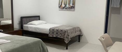 Habitación de hotel con dos camas, un escritorio, una silla, aire acondicionado y un espejo.