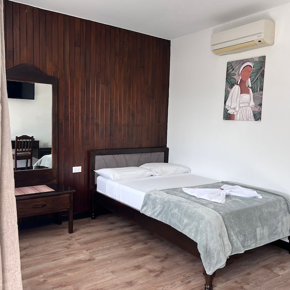 A bedroom with a wooden headboard, a bed with white linens, a grey blanket, a small bedside table, a chair, a mirror, an air conditioning unit, and a wall-mounted artwork. - Hotel Naralit (Tilaran)