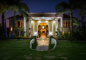 A well-lit entrance with a covered patio, palm trees, and a stone pathway leading to the door. - An Ultra-Luxurious Resort Style Ocean View Villa. Optional Yacht, Fully Staffed! (Discovery Bay)