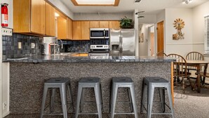 A modern kitchen with wooden cabinets, a granite countertop, stainless steel appliances, and a bar area with stools. - Amazing Sunset View on Canyon Lake! (Canyon Lake)