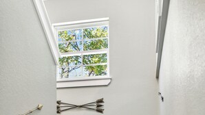 Una escalera de madera con paredes blancas y un ventanal con vistas a árboles.
