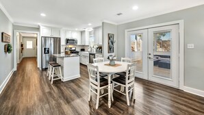 Una cocina moderna con muebles blancos, una isla central y un comedor con sillas blancas.