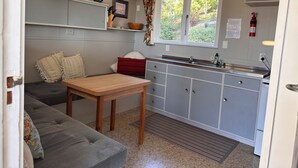 Eine kleine Küchenzeile mit Spüle, einem Fenster mit Vorhängen, einem Tisch und einer Couch.