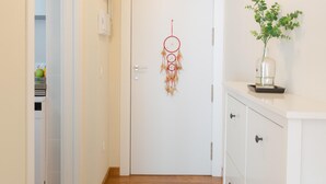 A hallway with a white door, a dreamcatcher, a plant in a glass vase, and a white cabinet with drawers. - Quiet apartment with a nice terrace (Málaga)