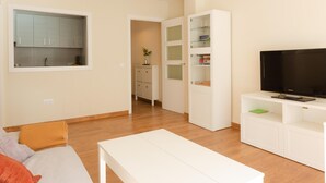 A modern living room with a flat-screen TV, white furniture, and a kitchen area visible through an open door. - Quiet apartment with a nice terrace (Málaga)