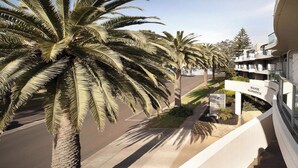 A modern building with a curved facade, palm trees lining the street, and a clear sky. - STYLISH ISLAND GETAWAY - BEACHFRONT APARTMENT - COWES - Phillip Island (Cowes)