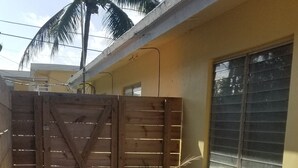 Una terraza de madera que lleva a una entrada con portón, con una palmera y una ventana al fondo.