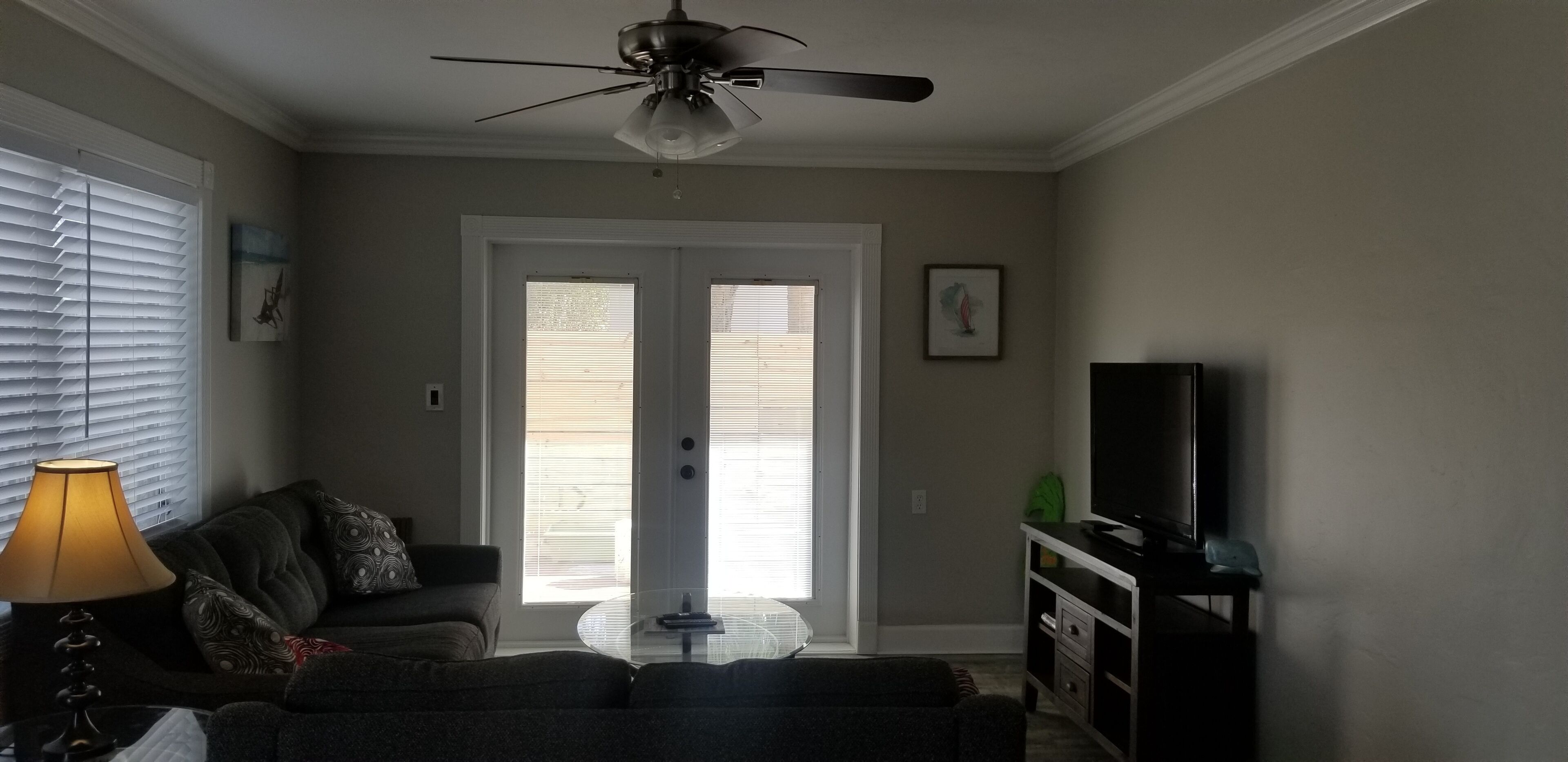 A living room with a ceiling fan, a sofa, a coffee table, a TV, and a lamp.